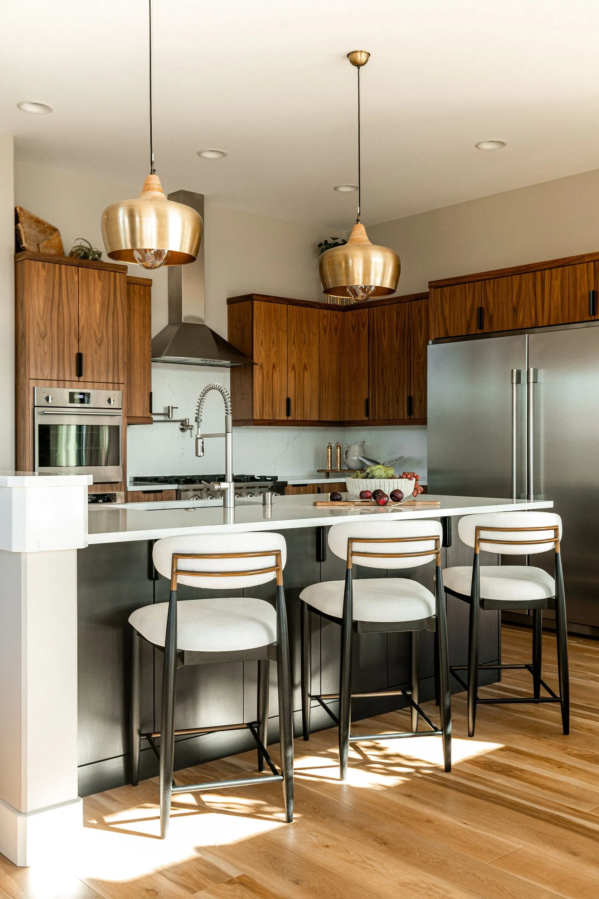 Walnut kitchen with a waterfall stone island, counter stools and brass pendants in a newly built home