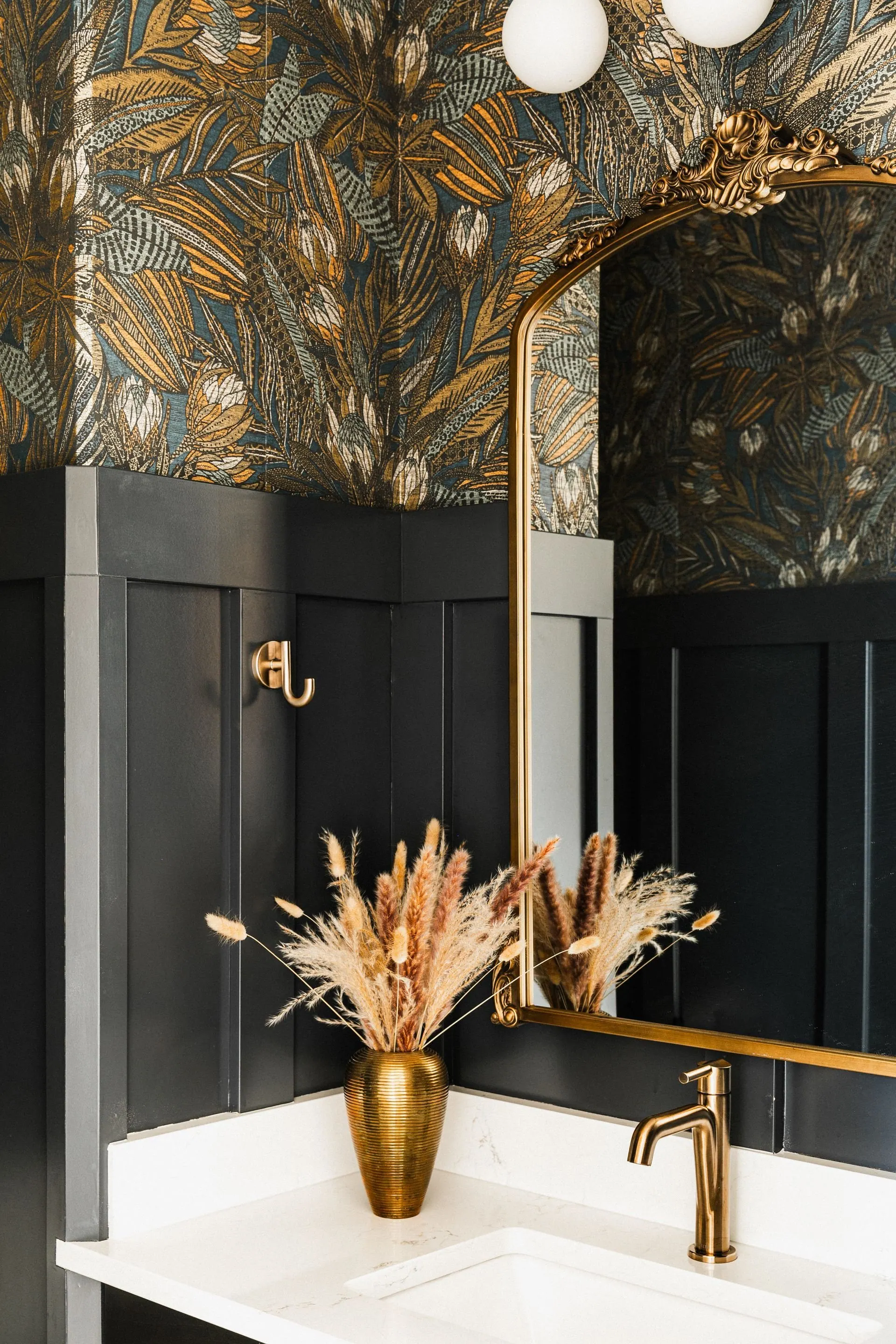 Powder room wrapped in botanical wallpaper above deep painted wainscot with a brass vanity