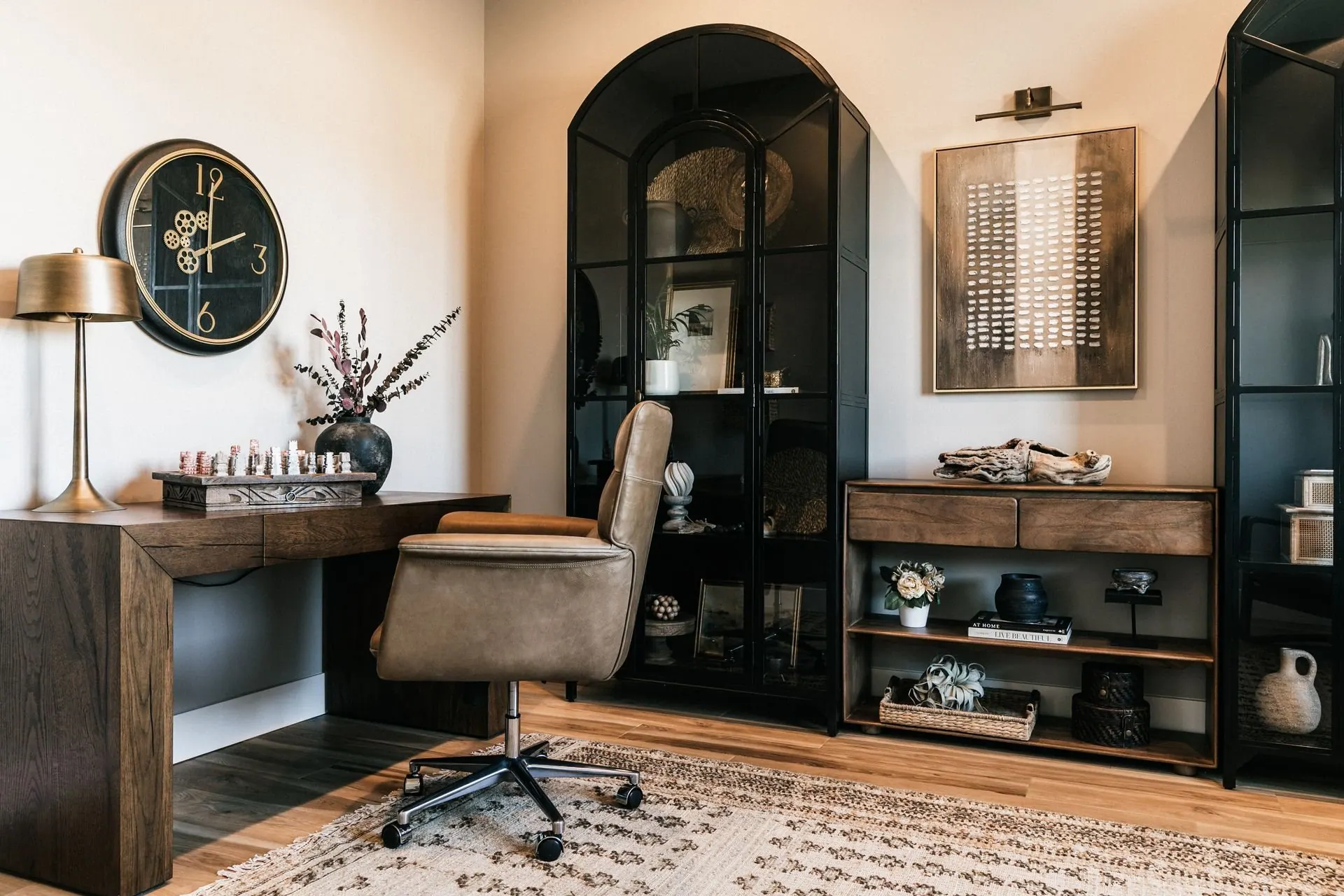 Home study with a wood desk, black arched display cabinets, and a patterned area rug