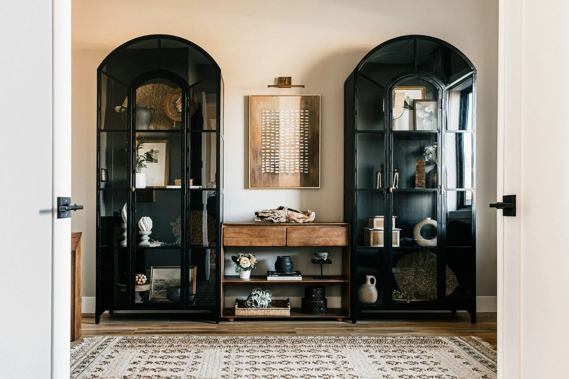 Black arched built-in display cabinets styled in layers with stacked books, ceramic vessels and small collected objects, with bare shelf left between the groupings