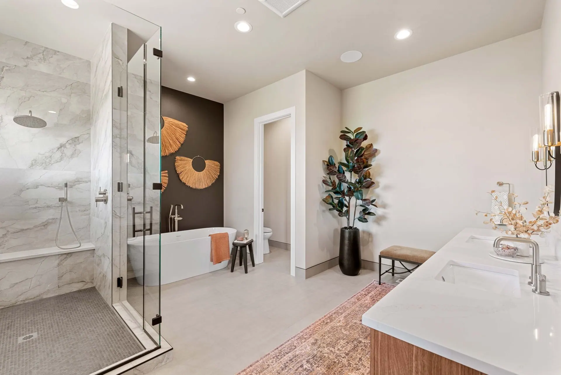 Walk in shower tiled floor to ceiling behind a frameless glass enclosure, with a patterned rug on the bathroom floor