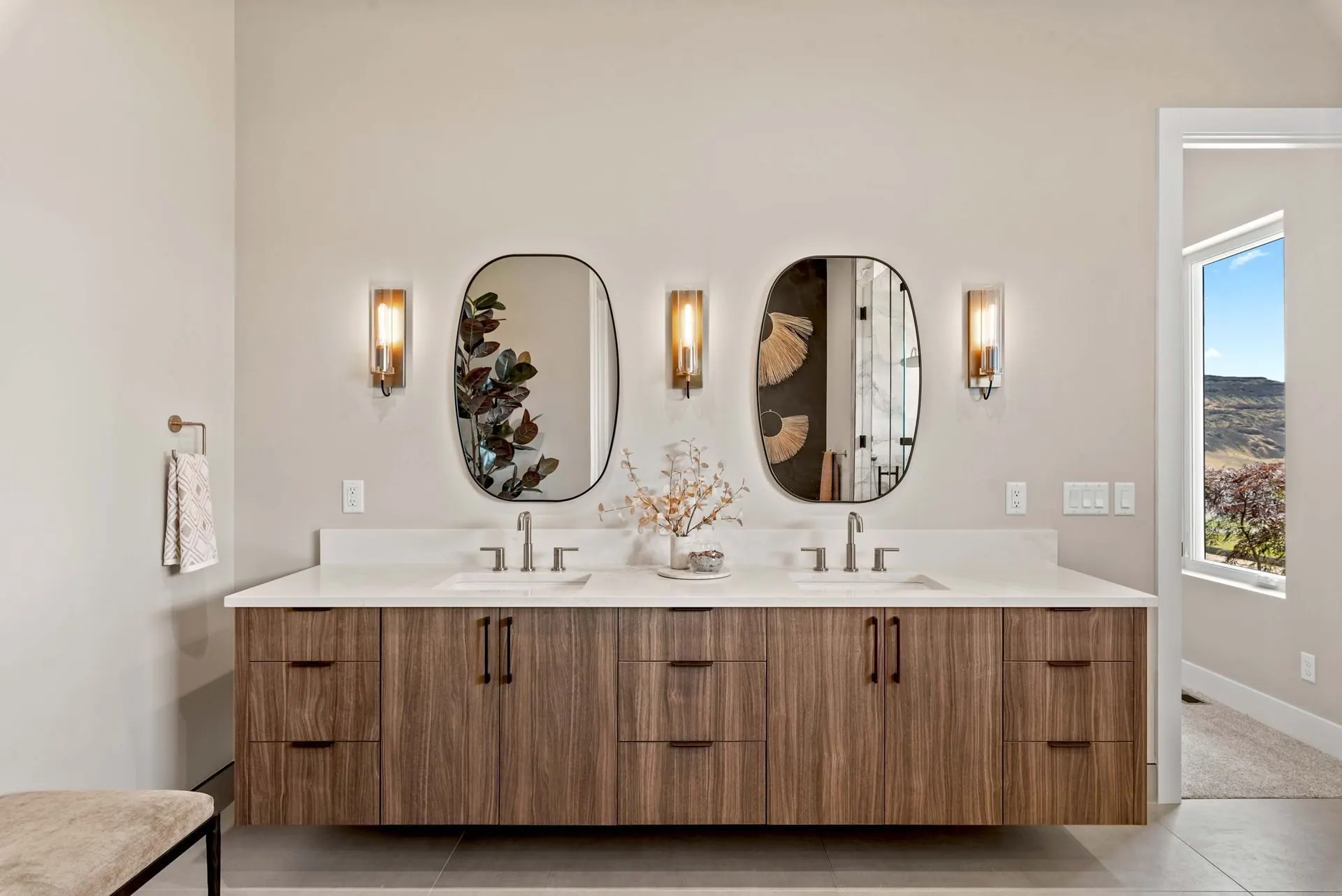 Primary bathroom double vanity with walnut cabinetry, arched mirrors and natural light