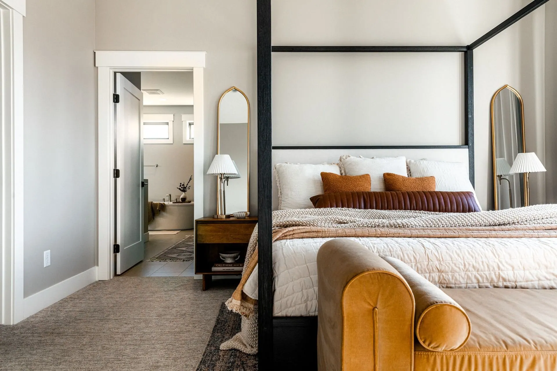 Bedroom with a canopy bed, ochre accent pillows, and an open view through to the ensuite bathroom