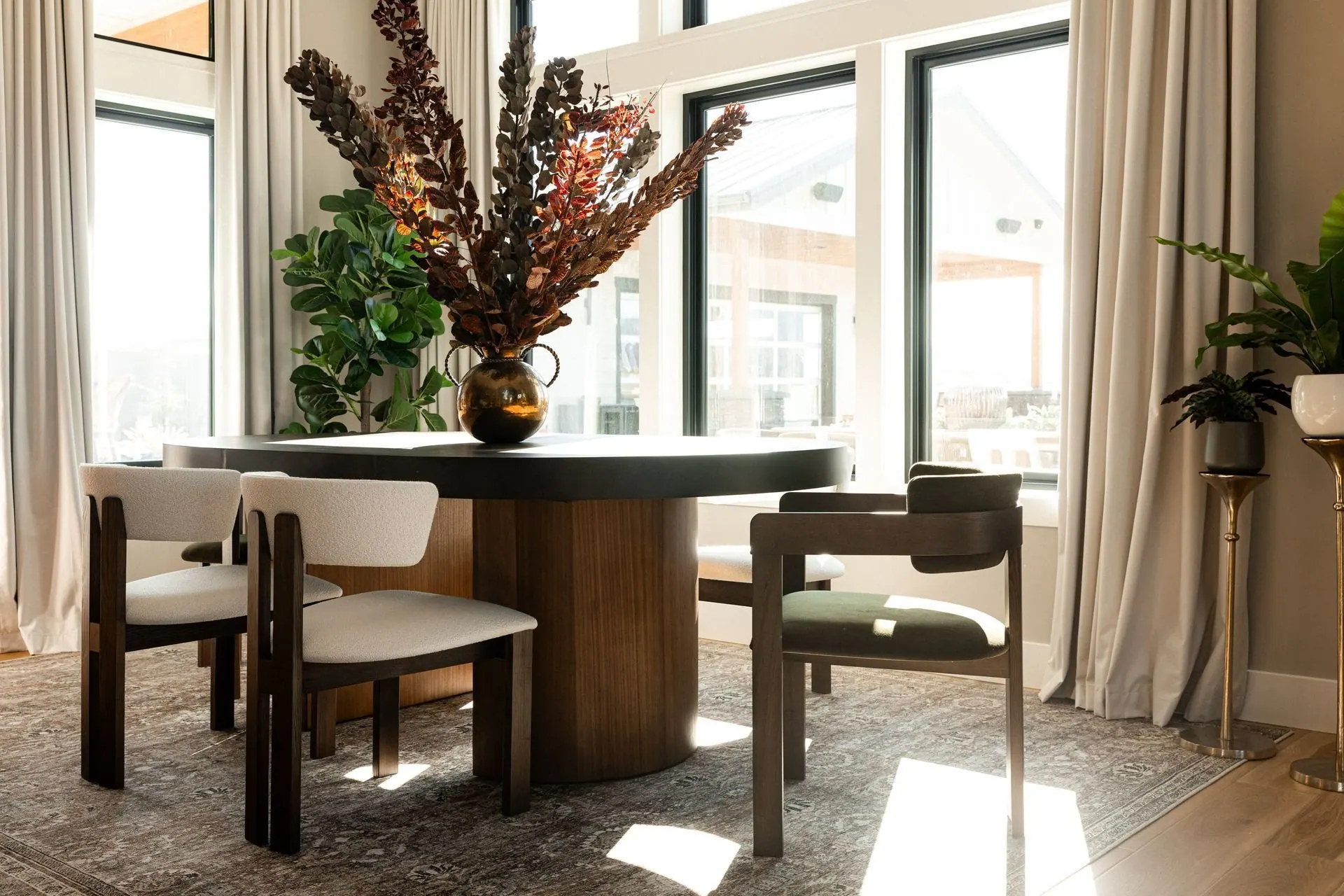 Dining nook with a dark round table, sculptural florals, and valley views framed by large windows