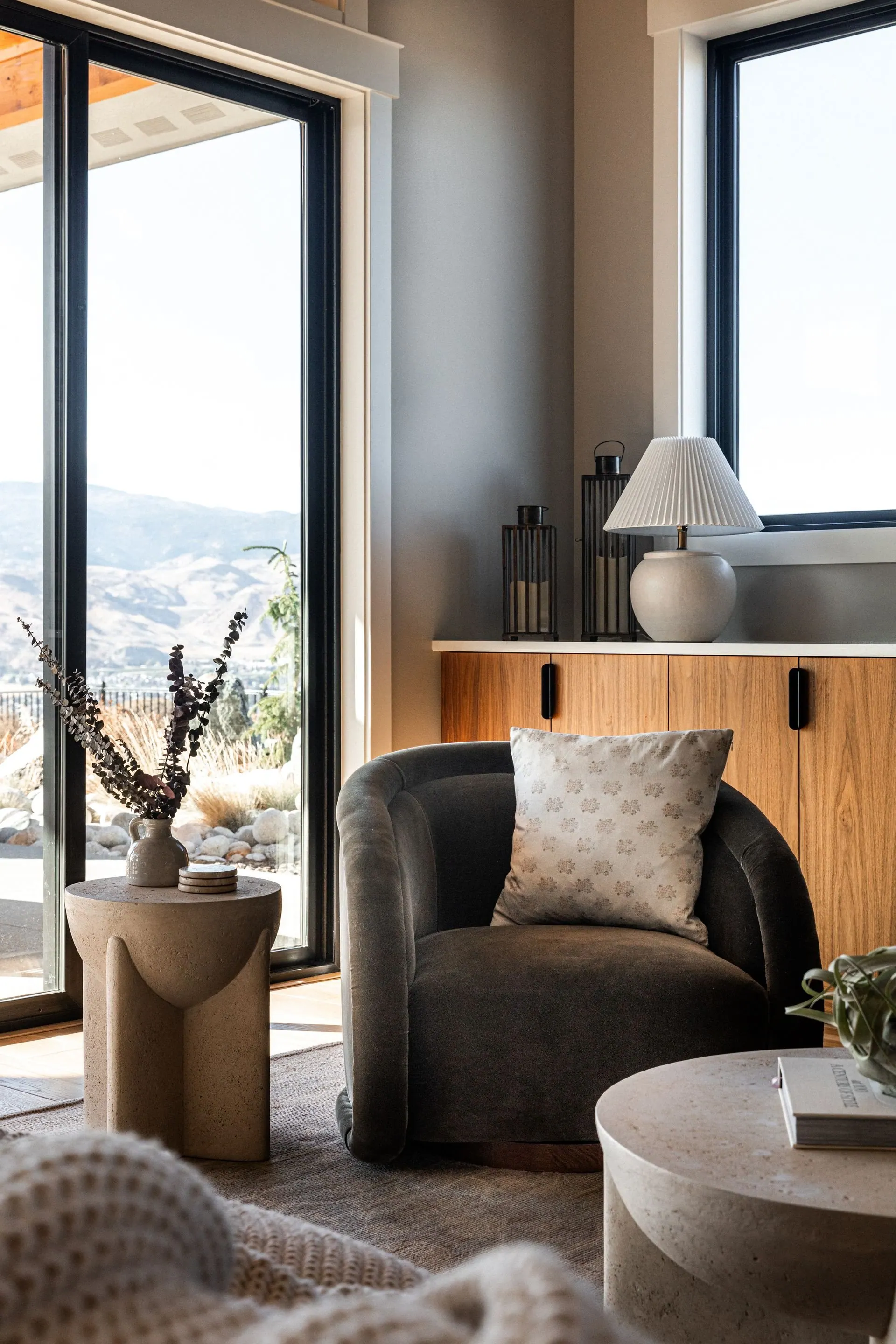 Reading corner with a swivel accent chair, side table and table lamp placed beside a window looking out to the valley