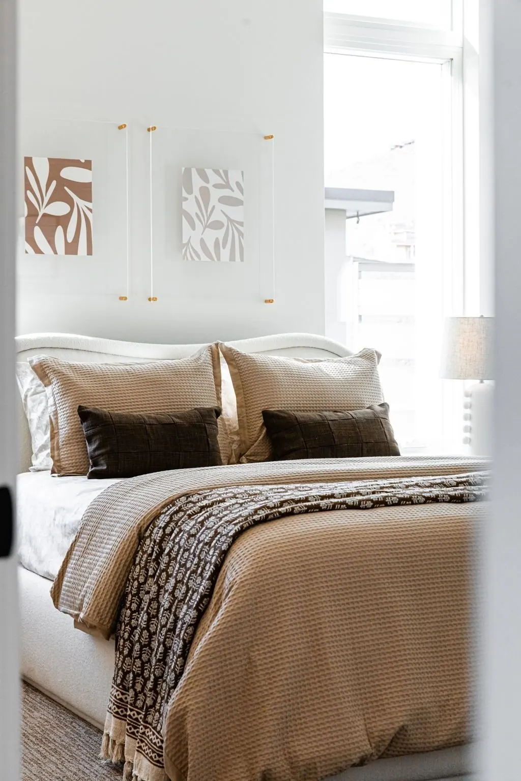 Bedroom dressed in layered neutral bedding with textured throws and a quiet piece of artwork above the bed