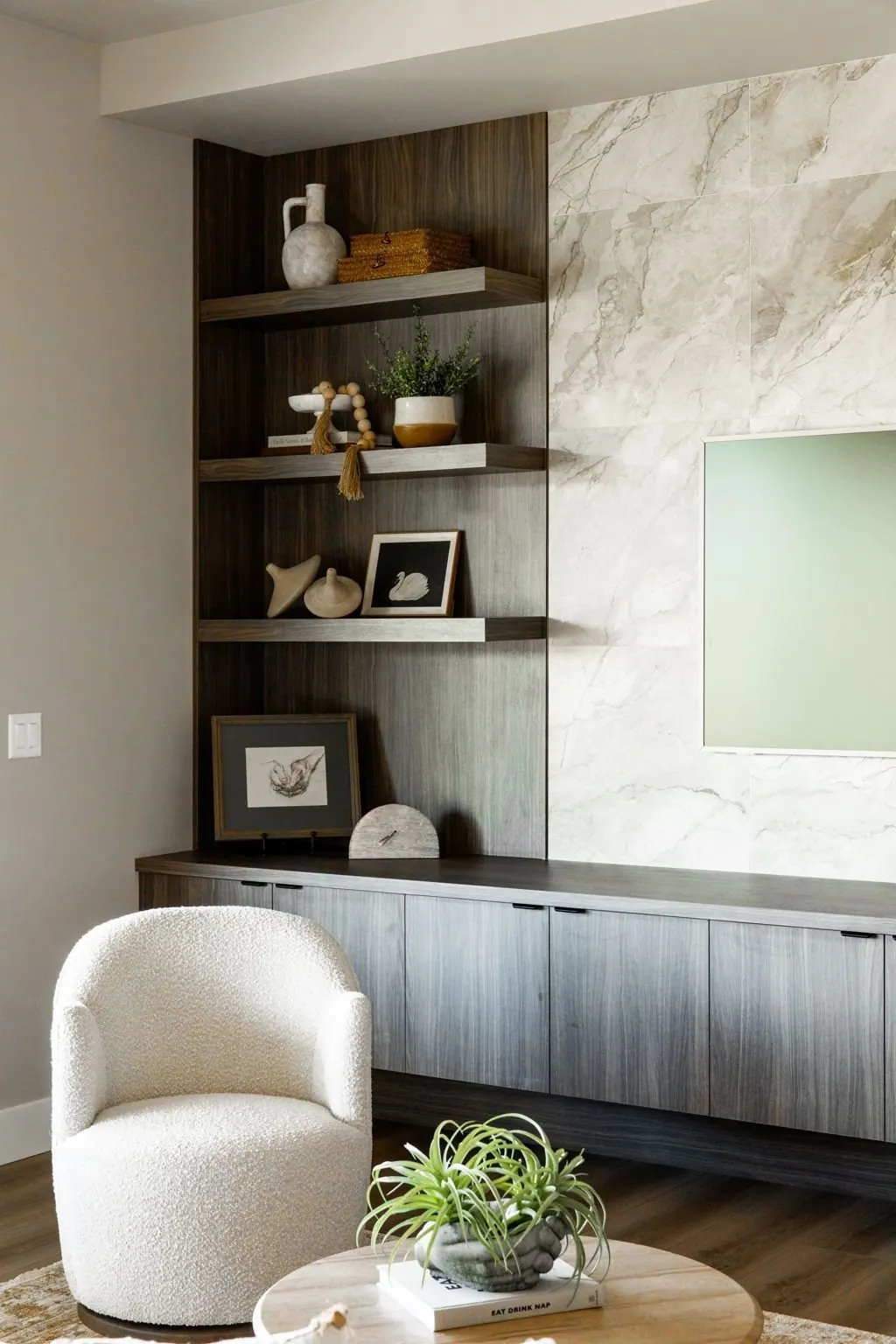Built-in wood shelving nook styled with books and objects beside a soft accent chair