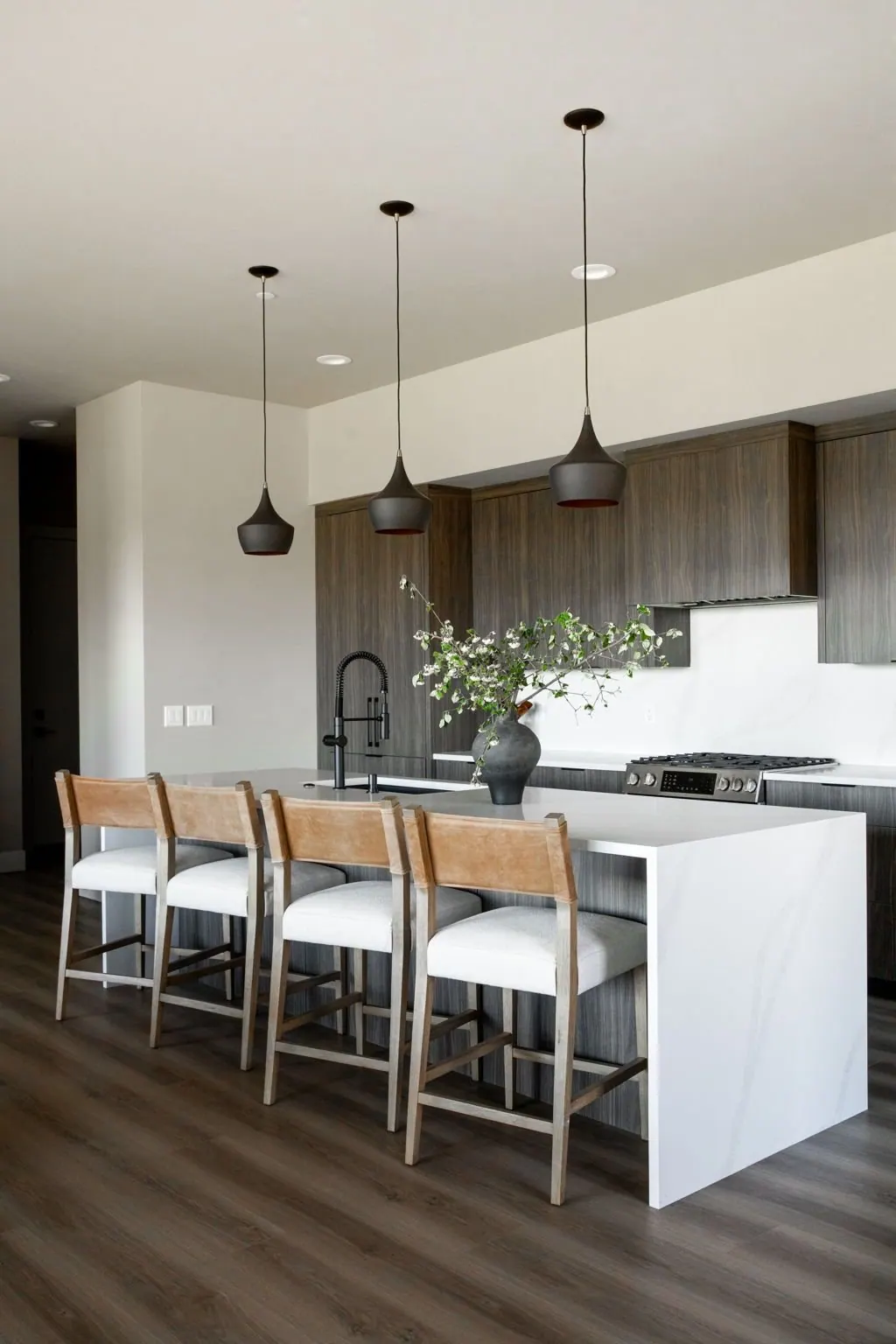 Kitchen island with wood counter stools and slim pendant lighting in a new construction home