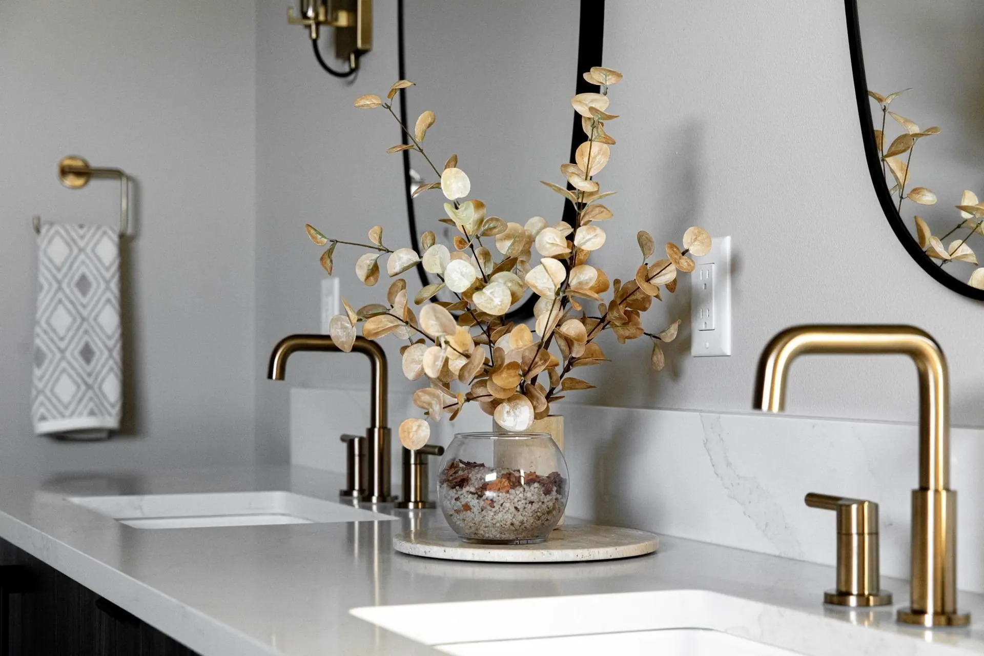 Vanity detail with a brass faucet, marble counter, and a sculptural floral arrangement