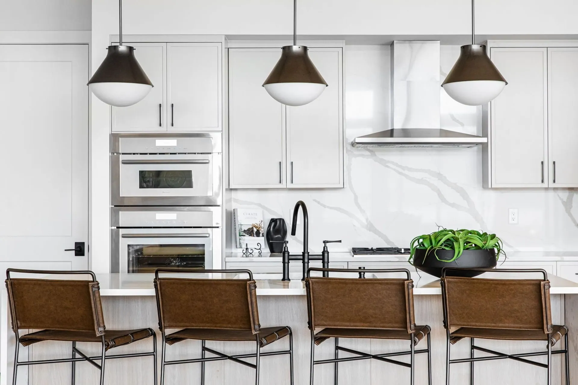 Renovated kitchen with white cabinetry, a marble backsplash, double wall ovens, and an island with wood counter stools
